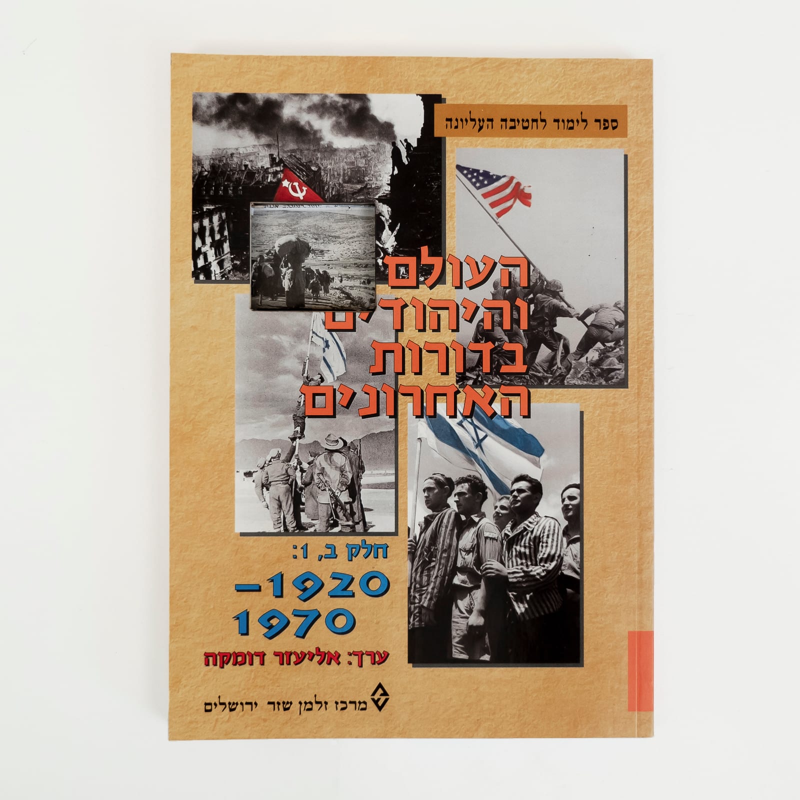 Photograph of an Israeli history textbook on a white background. The cover is a collage of mid 20th century photographs of war, liberation, and flag raising. A small rectangular cut in the top left area of the cover reveals a photograph from the 1948 Palestinian Nakba. The Hebrew title reads in orange and then blue, The World and the Jews in Recent Generations, Part B,1: 1920–1970.