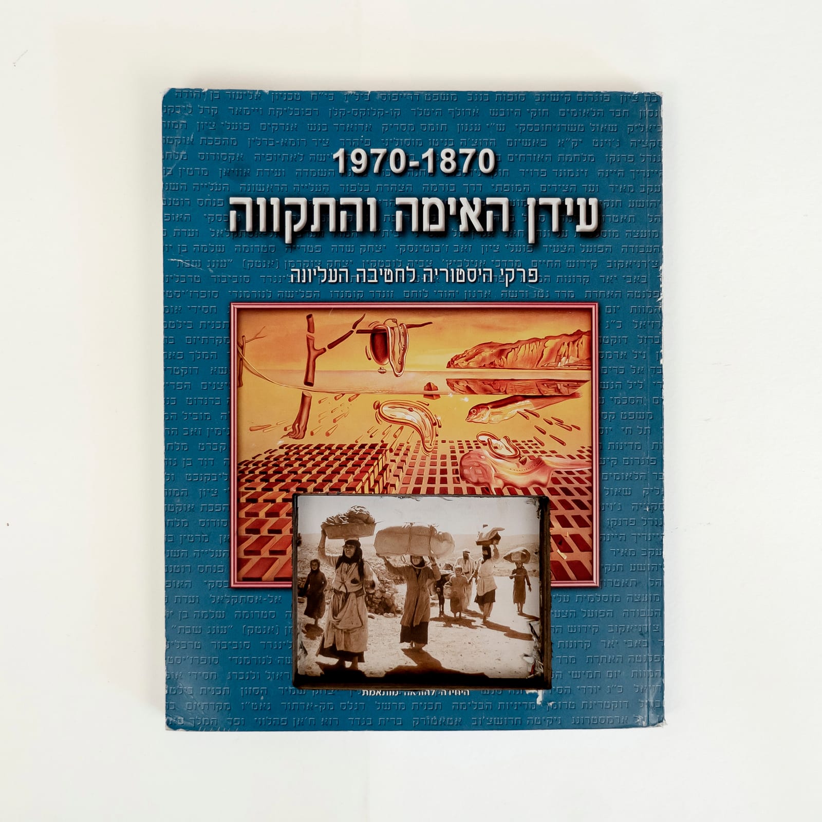 Photograph of a used Israeli history textbook against a white background. Hebrew title reads, The Age of Terror and Hope, 1870–1970. Below it a yellow monochrome version of Dalí's Persistence of Memory. Cut into the bottom of it and into the rest of the background is a rectangle revealing a photograph from deeper in the book of the 1948 Palestinian Nakba, people walking carrying some of their belongings. The rest of the cover is a solid blue with lines of small Hebrew text.
