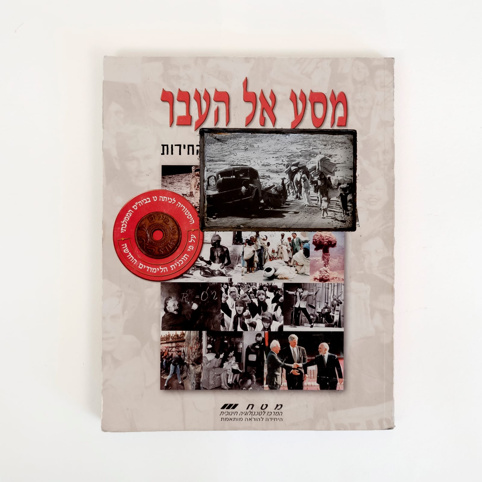 Photograph of an Israeli history textbook against a white background. The Hebrew title in red reads, Journey to the Past. Obscuring the subheading and the collage below it is a rectangular cut that reveals a photograph of the 1948 Palestinian Nakba from deep in the book: people walking on a dirt road next to a broken down car, carrying belongings. The collage depicts well known world leaders, historical events, and popular figures. A red circle with an image of a coin contains text about
